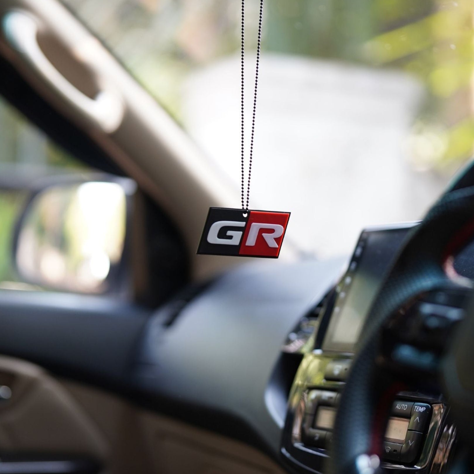 Car air freshener with 'GR' logo hanging from a car's rearview mirror.