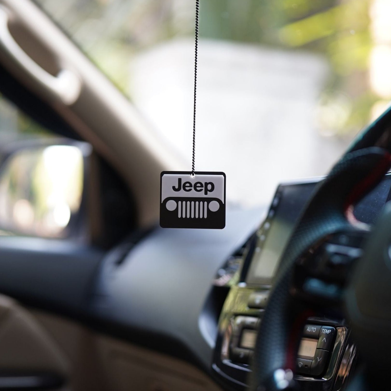 Jeep logo car air freshener hanging from a car's rearview mirror.