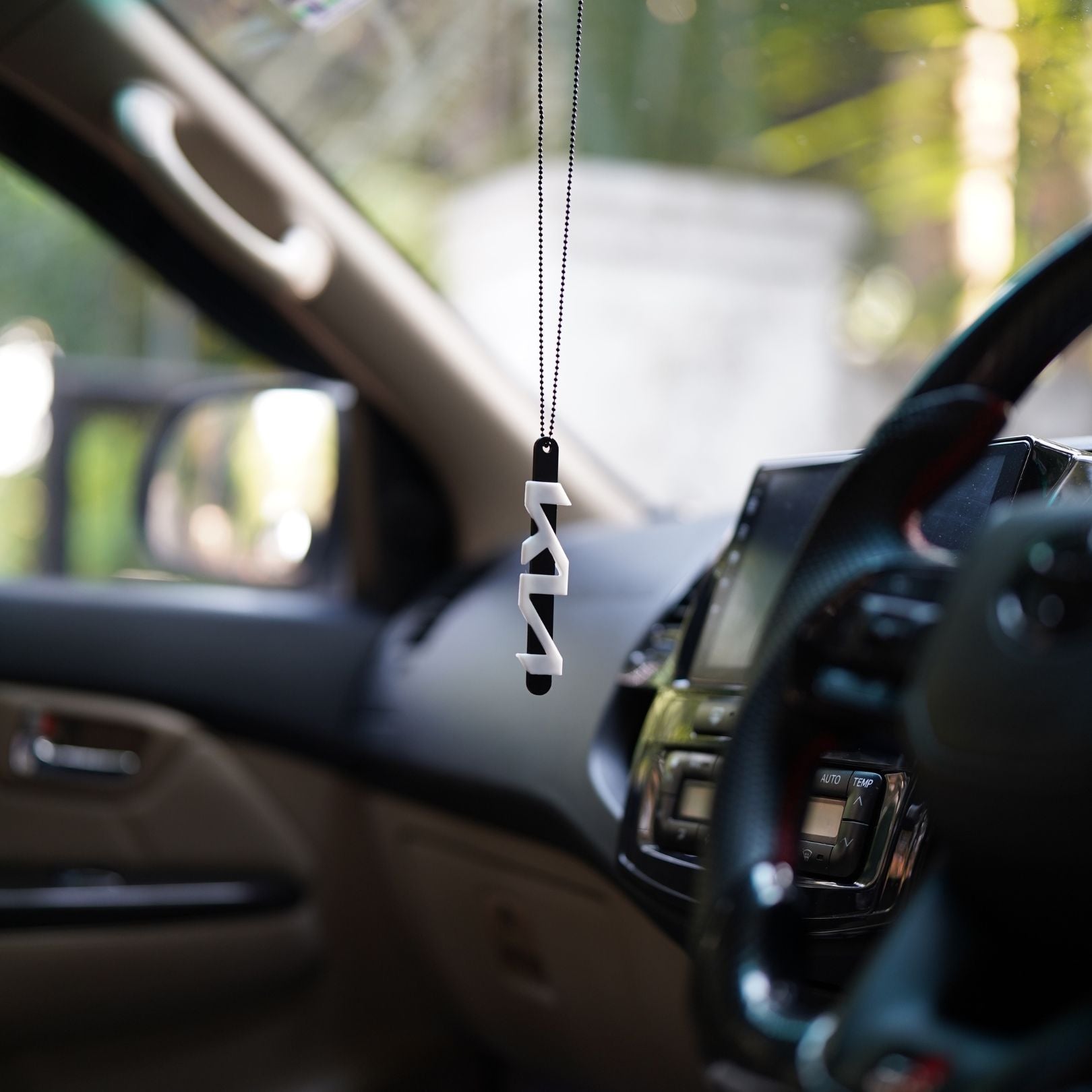 Car air freshener hanging from a car's rearview mirror with a blurred interior background