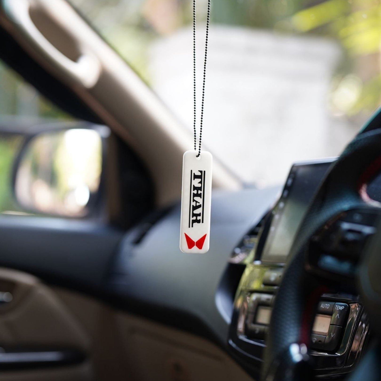 Car air freshener hanging from a car's rearview mirror with a blurred outdoor background
